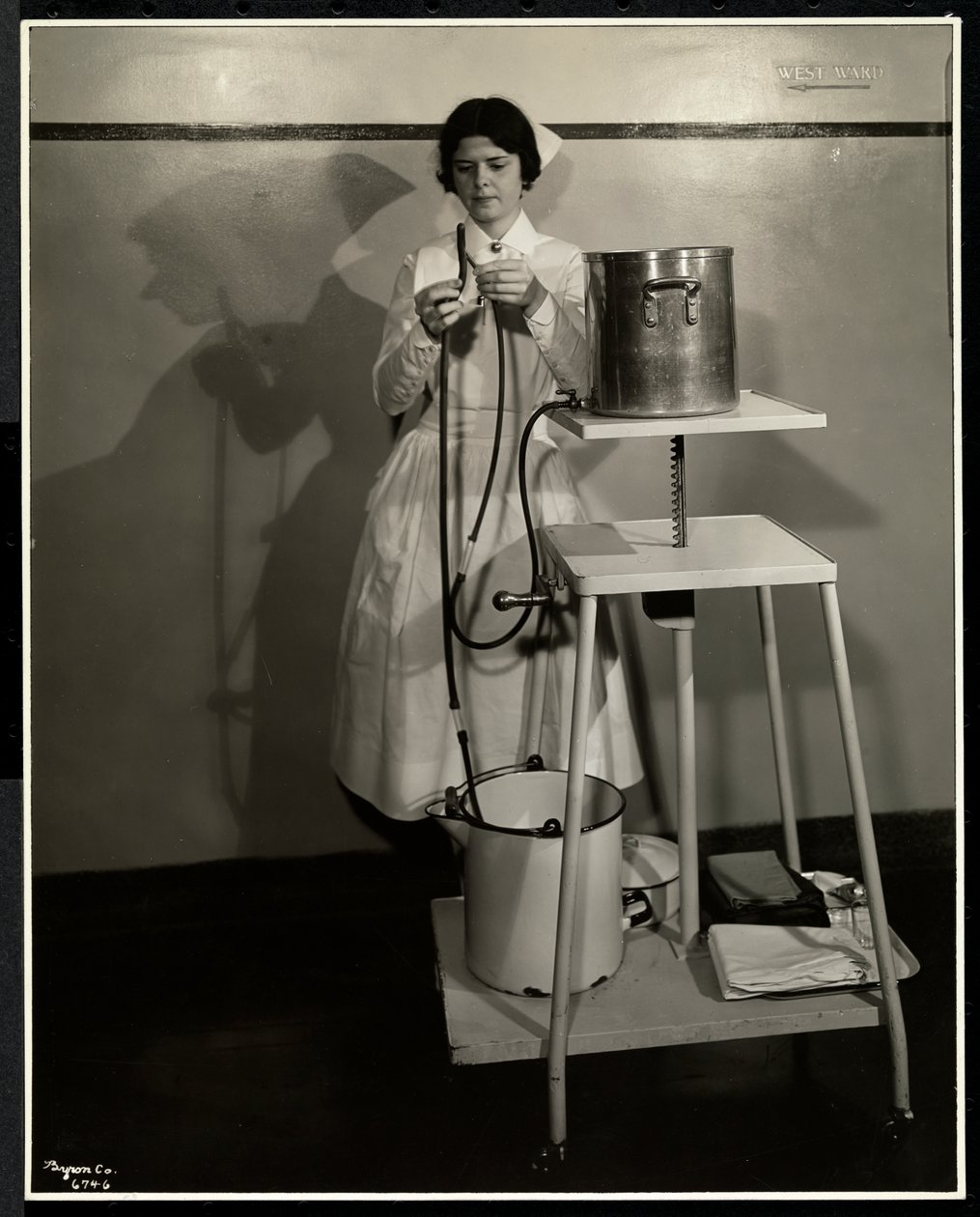 A nurse demonstrating a special apparatus with tubes and supply and refuse buckets at Sloan Maternity Hospital, Broadway and 168th Street, New York, 1932 by Byron Company