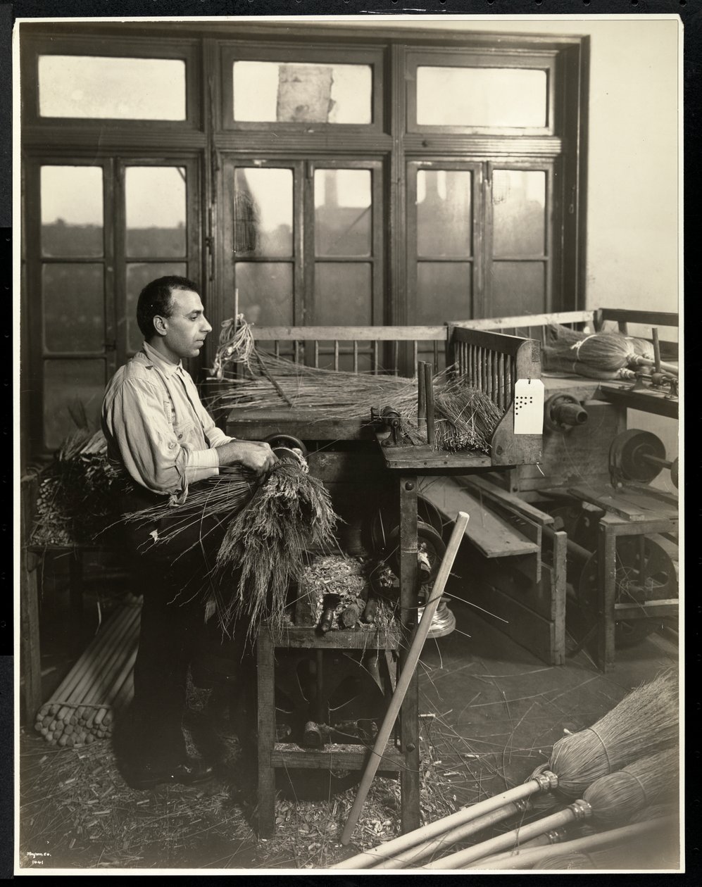 Blind man fastening straw on broom handles at the Bourne Memorial Building, New York, 1921 by Byron Company