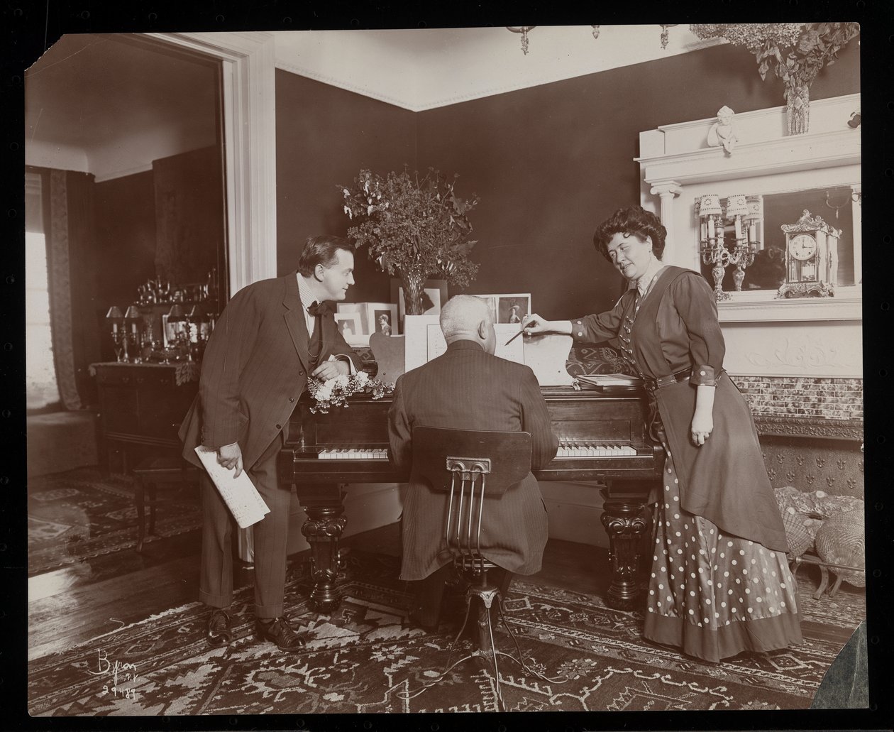 Clara De Regand pointing to a score while a man plays the piano by Byron Company