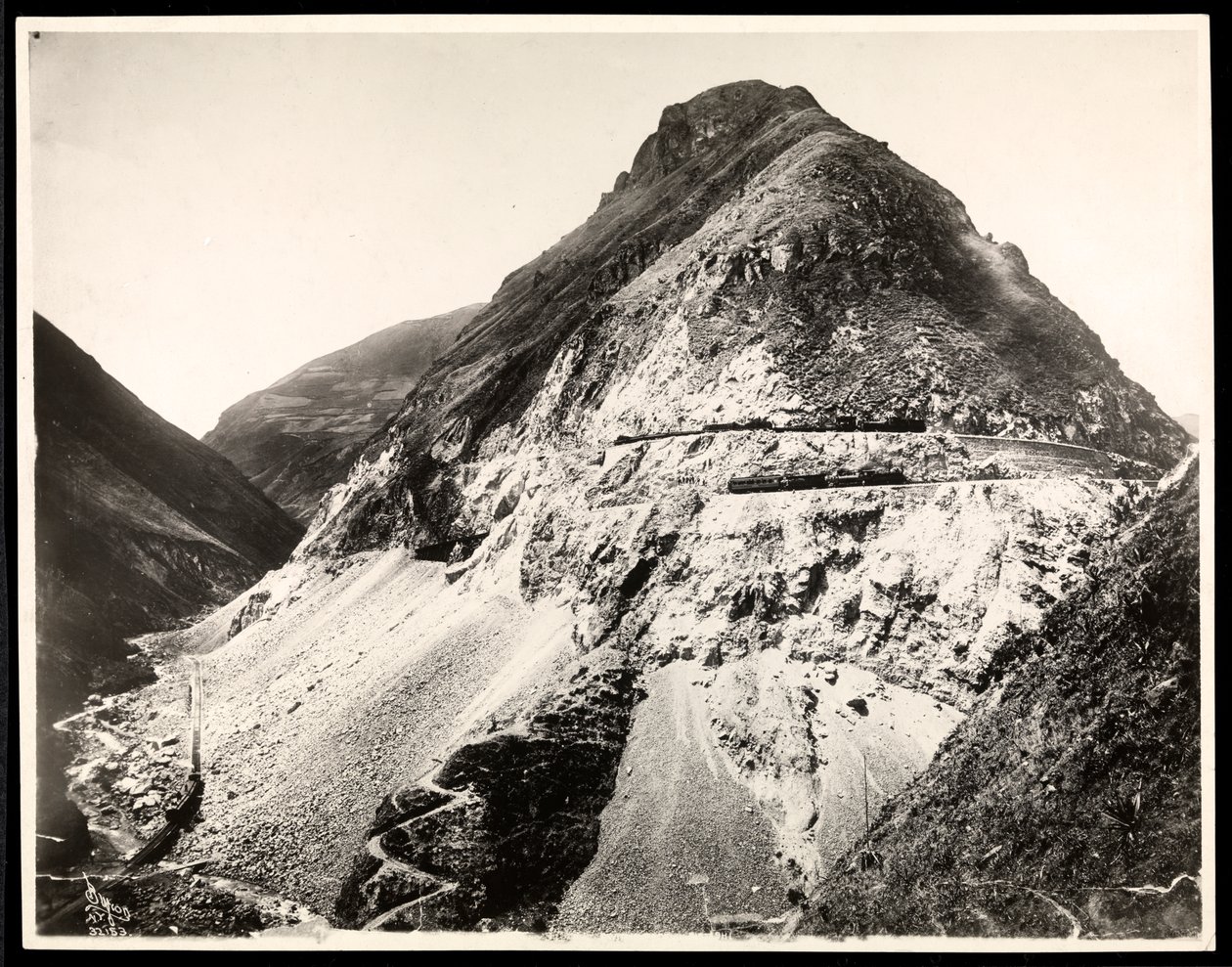 View of two railroad trains on tracks along a mountain, presumably on or near the Panama Canal by Byron Company