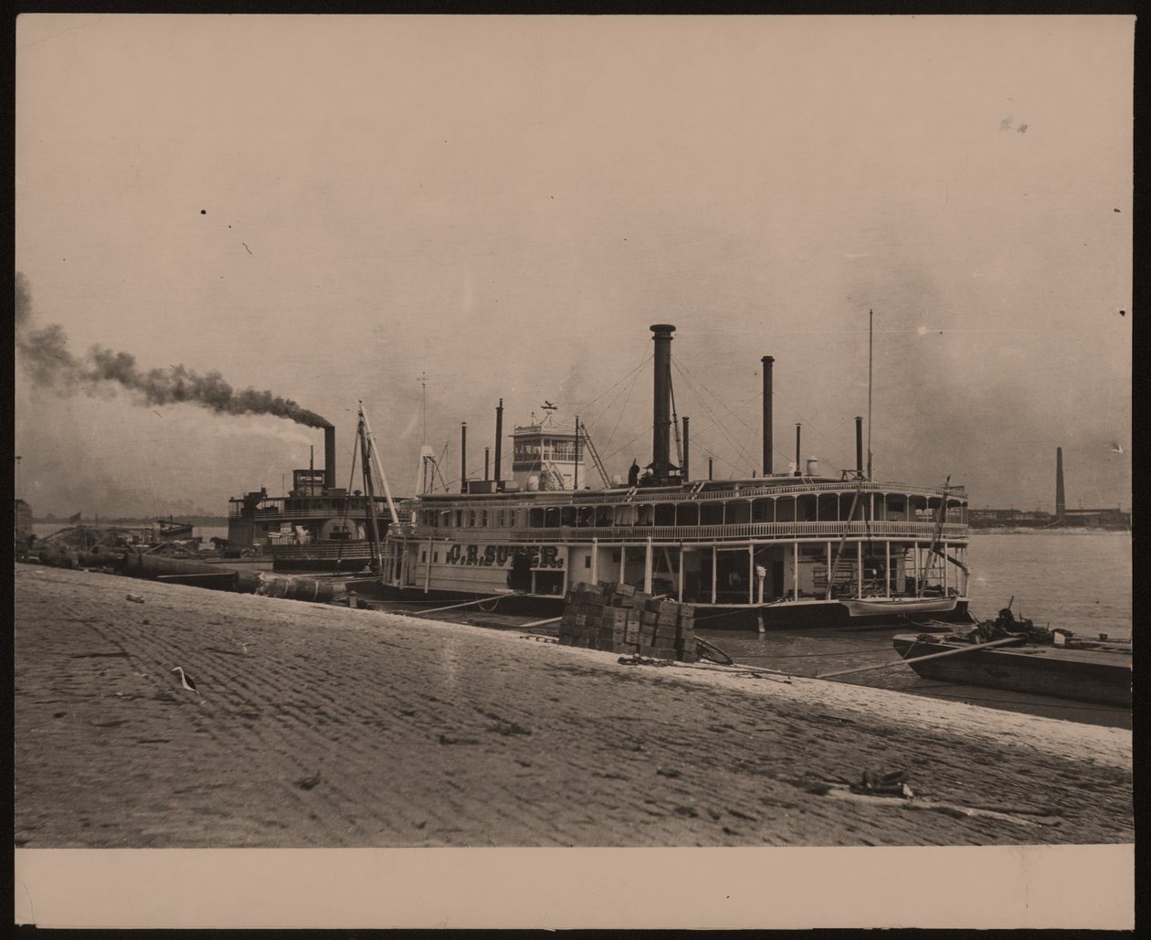 Horizontal, black and white photograph of the steamboat C.R. Suter. Another steamboat is parked behind it and crates are piled on the shore by William G. Swekosky